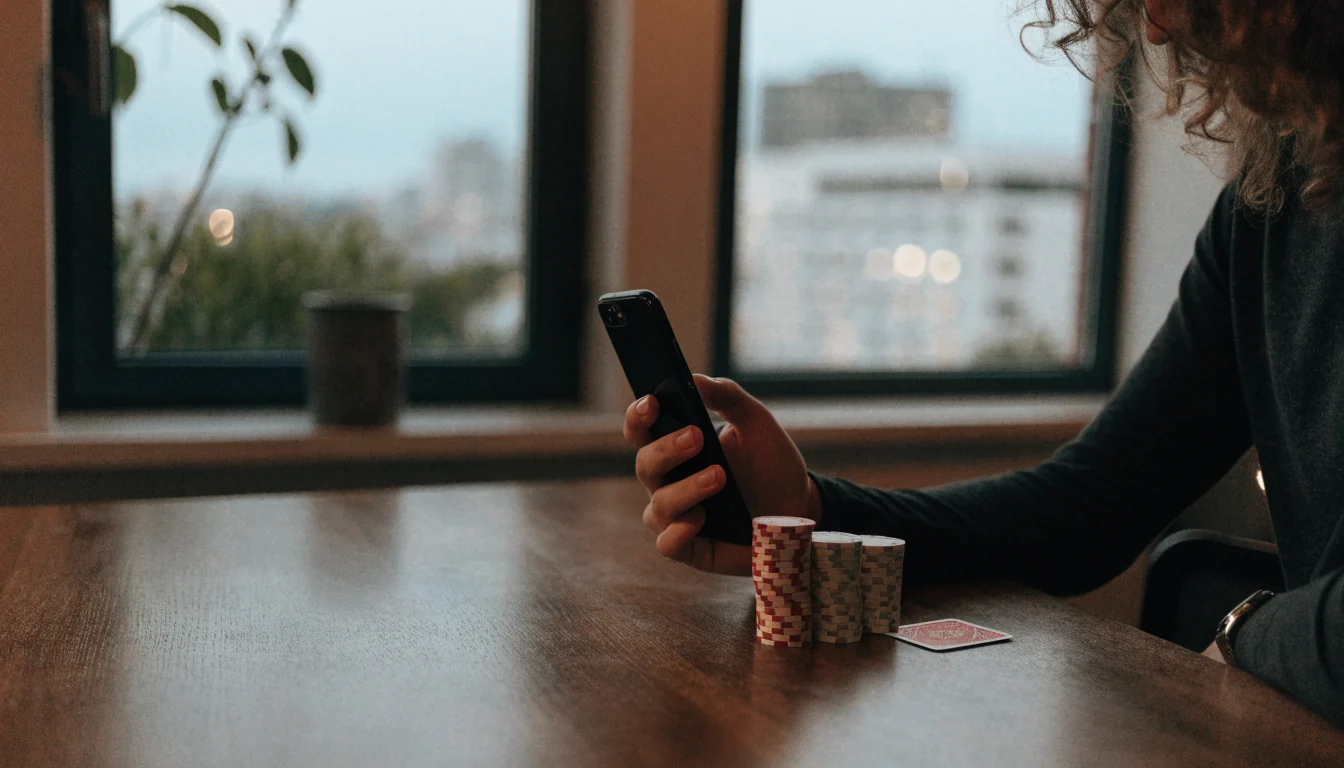 Person holding a smartphone near casino chips by a window in Auckland.